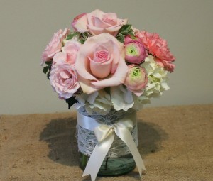 Pink roses and ranunculus with white hydrangea in a lace-wrapped vase