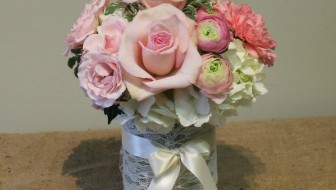 Pink roses and ranunculus with white hydrangea in a lace-wrapped vase