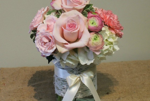 Pink roses and ranunculus with white hydrangea in a lace-wrapped vase